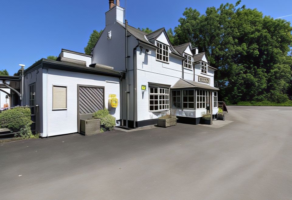 a white house with a sloping roof , surrounded by trees and parked cars on the street at Burlton Inn