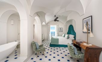a hotel room with a white bed , blue and white floor tiles , and a balcony overlooking the ocean at Hotel Miramalfi