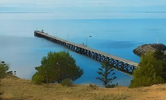 a long pier stretches out into the water , with trees and a person standing on it at Stansbury Holiday Motel