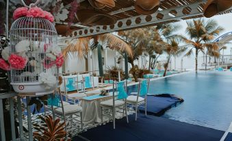 a poolside dining area with white chairs and blue tablecloths , surrounded by palm trees and a blue mattress at Ocean View Residence