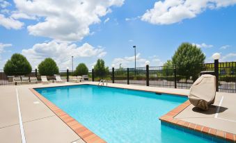 a large outdoor swimming pool surrounded by a fence , with lounge chairs and umbrellas placed around the pool area at Hampton Inn Lenoir City