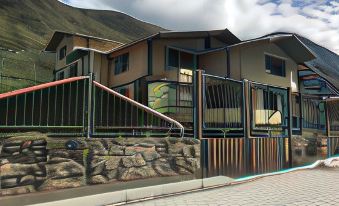 a modern building with stone walls and wooden railings , situated in front of a mountainous landscape under a cloudy sky at La Casa Verde