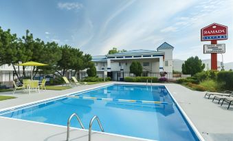 a large swimming pool with a white building and trees in the background , under a clear blue sky at Grand Forks Inn