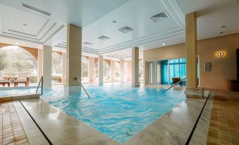 an indoor swimming pool with a rectangular design , surrounded by pillars and glass windows , allowing natural light to enter the space at Tikida Golf Palace
