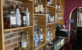 a well - stocked liquor cabinet with various bottles of alcohol , and a black counter with a cash register at The Ardingly Inn