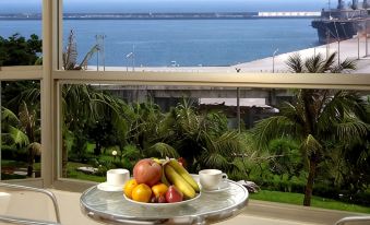 a dining table with a bowl of fruit sits on it , overlooking a body of water at Ocean Hotel