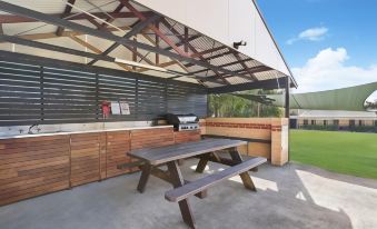 an outdoor kitchen with a grill , sink , and dining table under a covered area under a clear blue sky at Catalina Motel Lake Macquarie