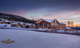 a large wooden building surrounded by snow - covered mountains , with a ski slope visible in the background at Mountain Lodge