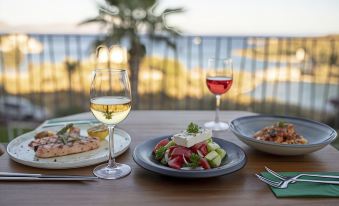 There is a table in the foreground filled with plates, glasses, and food, including wine at Cape Krio Boutique Hotel & Spa - over 9 Years Old Adult Only