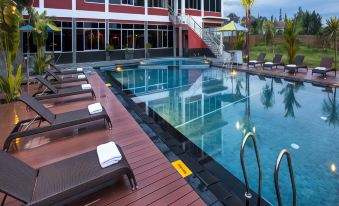 a large swimming pool with a wooden deck and lounge chairs is surrounded by red buildings at Merapi Merbabu Hotels Bekasi