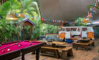 a tropical outdoor setting with a billiard table , benches , and a camper van under a large tent at Dreamtime Travellers Rest