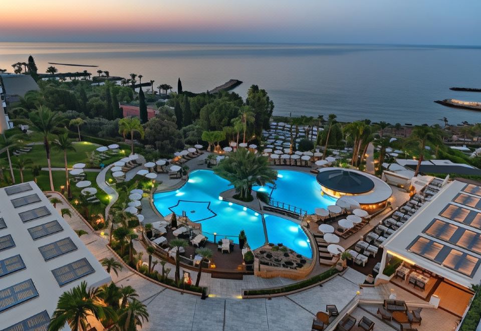 a large outdoor pool surrounded by lounge chairs and umbrellas , with a view of the ocean in the background at Mediterranean Beach Hotel