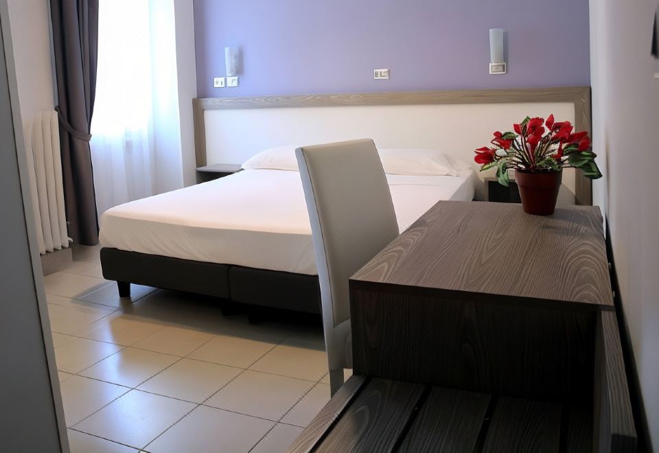 a bedroom with a bed and white linens , a desk with a vase of flowers , and two lamps on the wall at Hotel Savoia