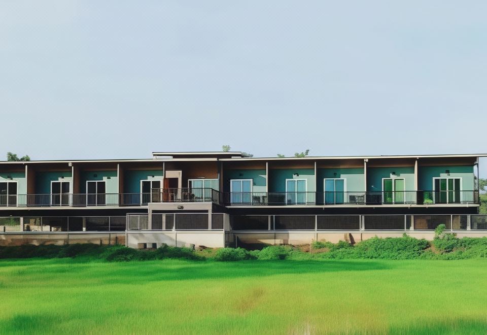 a modern , two - story building with green walls and large windows , surrounded by a lush green field at JC Resort
