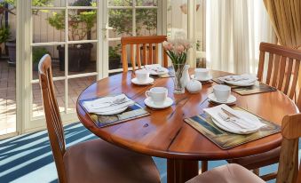 a wooden dining table with a wooden frame is set with plates , cups , and silverware at Durham Lodge Bed & Breakfast