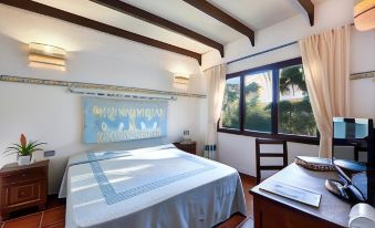 a bedroom with a large bed , wooden floor , and a window overlooking a garden area at Arbatax Park Resort - Telis