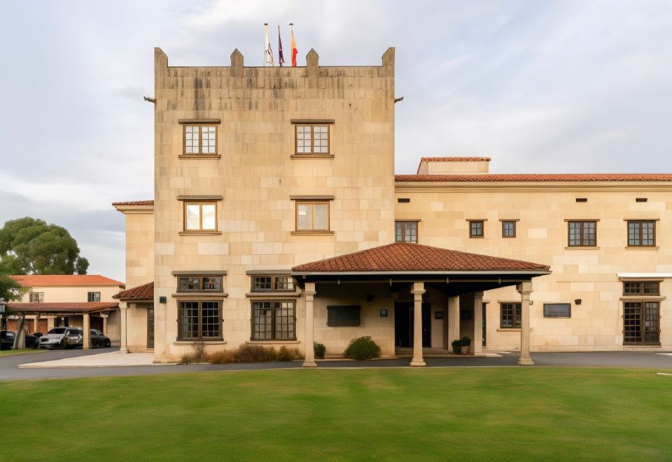 a large stone building with a red roof , surrounded by a grassy area and trees at Parador de Verin