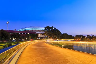 a large building with a curved roof is lit up at night , overlooking a city street at Oval Hotel at Adelaide Oval, an EVT hotel