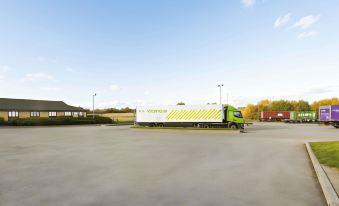 a green semi - truck is parked in a parking lot with a white and yellow van parked nearby at Days Inn by Wyndham Sutton Scotney South