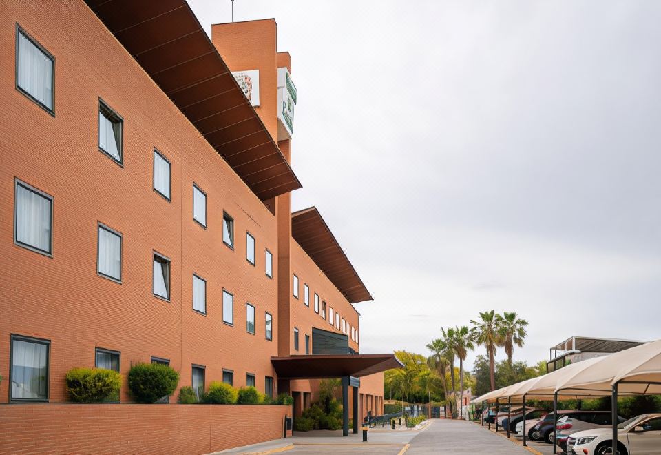 a brick building with a sign on the front , surrounded by cars parked in a parking lot at Posadas de Espana Malaga