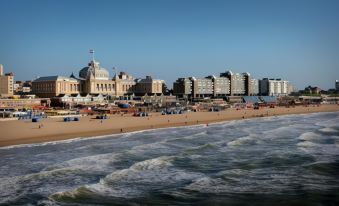 a beach scene with a large building in the background and people enjoying the sand and water at The Collector