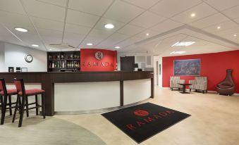 a red reception area with a black and white checkered floor , a red logo on the wall , and a black bar counter at Days Inn by Wyndham London Stansted Airport