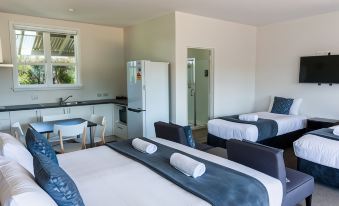 a modern bedroom with two beds , a dining table , and a kitchen in the background at North South Holiday Park