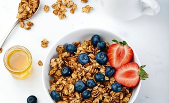 a bowl of granola with blueberries , strawberries , and honey is surrounded by milk and other breakfast items at Quality Hotel Grand Kongsberg