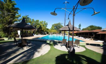 a large swimming pool surrounded by umbrellas and lounge chairs , with palm trees in the background at Hotel Fazenda Sete Lagos