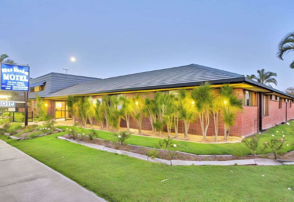 a modern building with brick walls and palm trees , surrounded by a well - maintained lawn and a grassy area at Blue Shades Motel