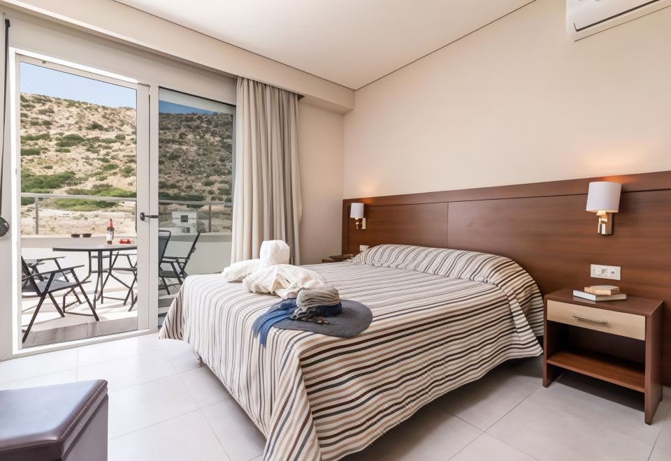 a bedroom with a bed , striped bedspread , and a window that offers a view of the outdoors at Matala Bay Hotel & Apartments