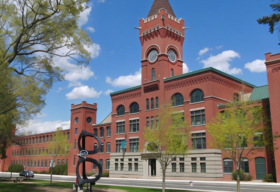 a large red brick building with a clock tower , surrounded by trees and a grassy area at Wellsworth Hotel