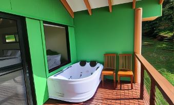 a green house with a wooden deck and two chairs , one of which is a white bathtub at Maleny Tropical Retreat