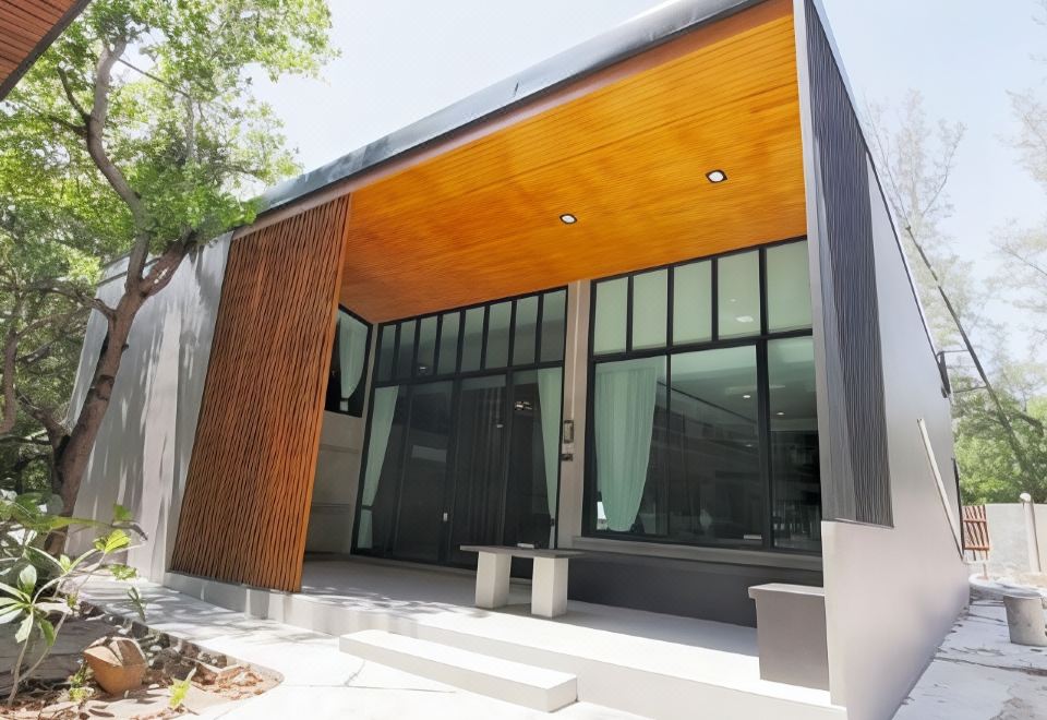 a modern house with a large window and wooden trim , located in a city setting at Baan Chao Mai Beach House