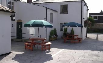 a courtyard with two picnic tables and umbrellas , providing shade for people to enjoy the outdoors at Thornton Hunt Inn