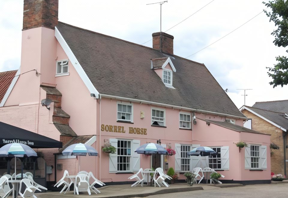 "a pink building with white shutters and a sign that says "" the sprockette "" has white umbrellas and chairs outside" at Sorrel Horse Inn