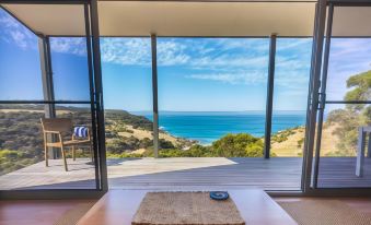 a wooden table with a placemat is placed in front of a large window overlooking the ocean at Sea Dragon Kangaroo Island
