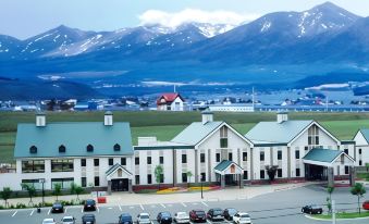a large white building with a green roof is situated in front of a mountain range at Furano la Terre