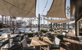 an outdoor dining area with tables and chairs arranged under a canopy , overlooking a body of water at Malibu Hotel