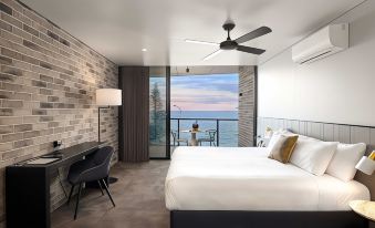 a modern bedroom with a large bed , desk , and sliding glass doors leading to a balcony overlooking the ocean at The Sebel Brisbane Margate Beach