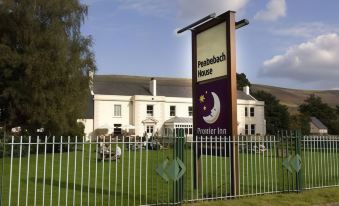 "a sign for the "" wellington hotel "" is displayed in front of a white building with a fence and green grass" at Premier Inn Merthyr Tydfil