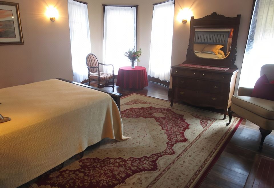 a well - decorated bedroom with a large rug , wooden furniture , and red and white floral rug at The Old Victorian Inn