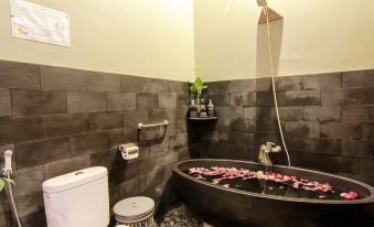 a modern bathroom with a black bathtub filled with water and flowers , a toilet , and a plant at Astuti Gallery Homestay