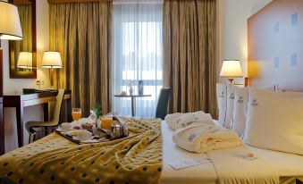 a well - arranged hotel room with a bed , curtains , and breakfast tray , along with two lamps on either side of the bed at VIP Executive Santa Iria Hotel