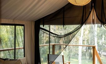 a modern tent interior with large windows , wooden furniture , and a bed decorated with white bedding at Paperbark Camp
