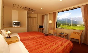 a hotel room with two beds , a tv , and a window offering a view of mountains at Hotel Hakuba