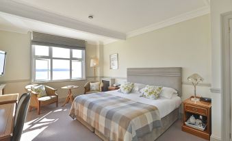 a large bed with a plaid blanket is in the middle of a room with two chairs and a window at Watersmeet Hotel