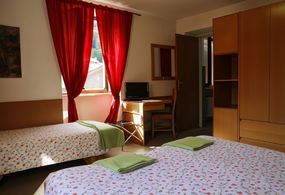 a bedroom with two beds , a desk , and a window with red curtains , decorated with floral bedding at Hotel Alpino