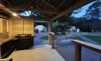 a large wooden patio with a grill and an outdoor kitchen , surrounded by trees and grass at Zeehan Bush Camp