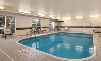 a large swimming pool with a curved edge and chairs around it , surrounded by a white tiled floor at Country Inn & Suites by Radisson, Toledo, Oh